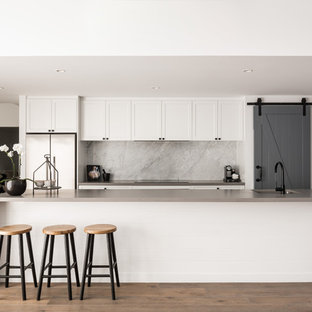 Transitional galley kitchen in Perth with an undermount sink, shaker cabinets, white cabinets, grey splashback, stone slab splashback, stainless steel appliances, medium hardwood floors, with island, brown floor and grey benchtop.