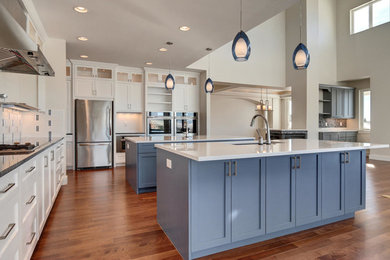 Inspiration for a large craftsman l-shaped light wood floor open concept kitchen remodel in Denver with an undermount sink, recessed-panel cabinets, blue cabinets, solid surface countertops, multicolored backsplash, ceramic backsplash, stainless steel appliances and two islands
