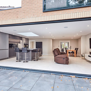 Inspiration for a mid-sized contemporary single-wall open plan kitchen in Other with an integrated sink, flat-panel cabinets, grey cabinets, quartzite benchtops, metallic splashback, mirror splashback, black appliances, porcelain floors, with island, grey floor, grey benchtop and vaulted.