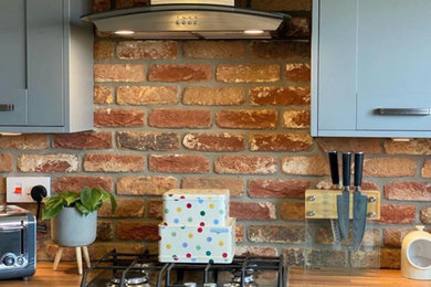 This is an example of a small rustic single-wall kitchen/diner in Other with shaker cabinets, grey cabinets, wood worktops, brick splashback, integrated appliances, an island and a double-bowl sink.