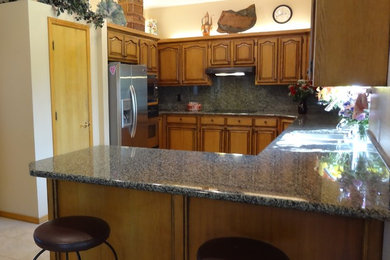 Mid-sized arts and crafts u-shaped kitchen photo in Boise with an undermount sink, raised-panel cabinets, distressed cabinets, granite countertops, black backsplash, glass sheet backsplash, stainless steel appliances and an island