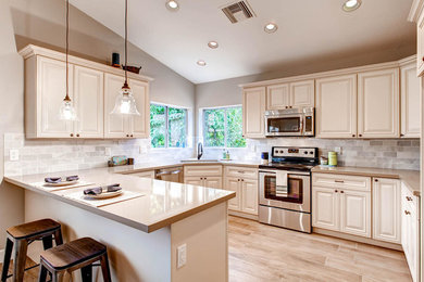 Foto på ett mellanstort amerikanskt kök, med en undermonterad diskho, luckor med upphöjd panel, vita skåp, bänkskiva i kvartsit, grått stänkskydd, stänkskydd i cementkakel, rostfria vitvaror, ljust trägolv, en köksö och beiget golv