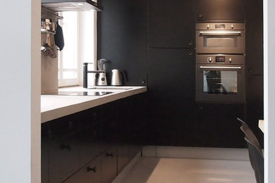 Foto de cocina actual de tamaño medio con fregadero encastrado, armarios con paneles lisos, puertas de armario negras, encimera de cemento, salpicadero verde, electrodomésticos negros y suelo de cemento