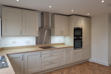 Inspiration for a medium sized contemporary l-shaped kitchen/diner in London with an integrated sink, shaker cabinets, grey cabinets, laminate countertops, metallic splashback, black appliances, vinyl flooring, no island, brown floors and brown worktops.