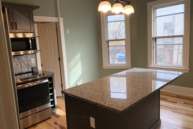 This is an example of a small traditional l-shaped kitchen in Burlington with a submerged sink, raised-panel cabinets, brown cabinets, granite worktops, metal splashback, stainless steel appliances, light hardwood flooring, an island and grey worktops.