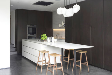 Inspiration for an expansive contemporary l-shaped kitchen/diner in London with a submerged sink, flat-panel cabinets, dark wood cabinets, marble worktops, white splashback, marble splashback, concrete flooring, an island, grey floors, black appliances and white worktops.