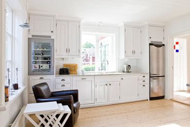 Klassische Küche mit Unterbauwaschbecken, Granit-Arbeitsplatte, Küchenrückwand in Weiß, Rückwand aus Keramikfliesen, Küchengeräten aus Edelstahl und hellem Holzboden in Stockholm