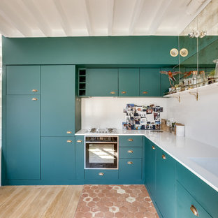 Idée de décoration pour une grand cuisine ouverte design en L avec des portes de placards vertess, aucun îlot, un évier intégré, un placard à porte plane, une crédence blanche, un électroménager noir, un sol en bois clair, un plan de travail blanc et un sol marron.