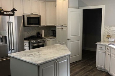 Example of a mid-sized transitional u-shaped dark wood floor and brown floor enclosed kitchen design in New Orleans with an island, raised-panel cabinets, white cabinets, granite countertops, gray backsplash, marble backsplash and stainless steel appliances
