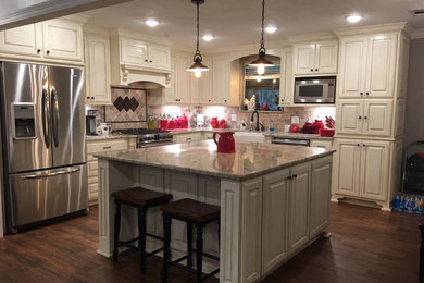 Example of a mid-sized classic l-shaped dark wood floor and brown floor enclosed kitchen design in New Orleans with a farmhouse sink, raised-panel cabinets, white cabinets, granite countertops, brown backsplash, stainless steel appliances and an island