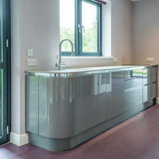 Offene, Einzeilige, Mittelgroße Moderne Küche mit Einbauwaschbecken, flächenbündigen Schrankfronten, lila Schränken, Mineralwerkstoff-Arbeitsplatte, Elektrogeräten mit Frontblende, braunem Holzboden, Kücheninsel, buntem Boden und weißer Arbeitsplatte in Cheshire
