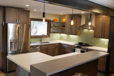 Inredning av ett modernt litet kök, med en undermonterad diskho, släta luckor, skåp i mellenmörkt trä, bänkskiva i betong, grönt stänkskydd, stänkskydd i glaskakel, rostfria vitvaror, ljust trägolv och en köksö
