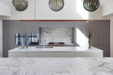 Modern inredning av ett stort linjärt kök med öppen planlösning, med en integrerad diskho, släta luckor, gröna skåp, marmorbänkskiva, grått stänkskydd, stänkskydd i marmor, svarta vitvaror, ljust trägolv, flera köksöar och brunt golv