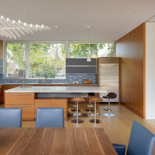 Modelo de cocina comedor en L, minimalista, con fregadero bajoencimera, armarios con puertas mallorquinas, puertas de armario de madera oscura, encimera de mármol, salpicadero azul, salpicadero de azulejos de cerámica, electrodomésticos de acero inoxidable, suelo de madera en tonos medios, una isla, suelo marrón y encimeras blancas