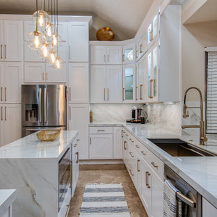 Large modern l-shaped eat-in kitchen in Houston with an undermount sink, shaker cabinets, white cabinets, solid surface benchtops, white splashback, porcelain splashback, stainless steel appliances, marble floors, with island, beige floor and white benchtop.