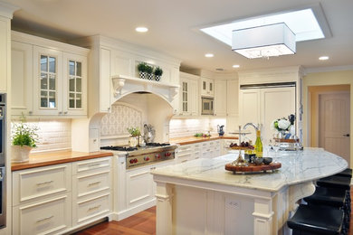 Eat-in kitchen - traditional l-shaped eat-in kitchen idea in Phoenix with a farmhouse sink, raised-panel cabinets, white cabinets, wood countertops, white backsplash, subway tile backsplash and paneled appliances