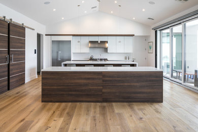 Expansive contemporary single-wall open plan kitchen in Phoenix with a submerged sink, flat-panel cabinets, dark wood cabinets, engineered stone countertops, white splashback, stainless steel appliances, light hardwood flooring, multiple islands, brown floors and white worktops.