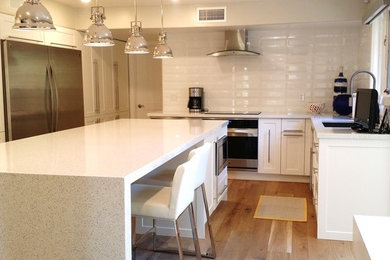 Example of a large trendy u-shaped light wood floor and brown floor eat-in kitchen design in Phoenix with an undermount sink, shaker cabinets, white cabinets, quartzite countertops, white backsplash, ceramic backsplash, stainless steel appliances and an island