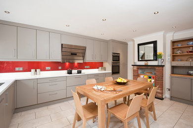 Photo of a medium sized contemporary l-shaped kitchen/diner in Hertfordshire with a submerged sink, flat-panel cabinets, grey cabinets, composite countertops, red splashback, glass sheet splashback, stainless steel appliances, ceramic flooring, no island and grey floors.