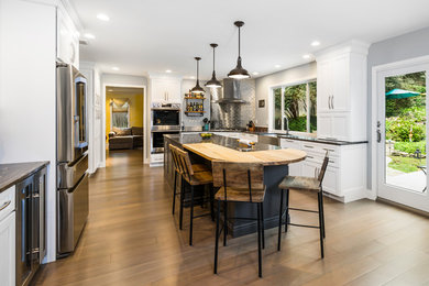 Kitchen - transitional l-shaped medium tone wood floor kitchen idea in Philadelphia with a farmhouse sink, recessed-panel cabinets, white cabinets, metallic backsplash, metal backsplash, stainless steel appliances, an island and black countertops