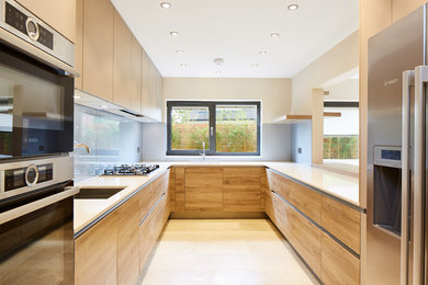 Contemporary u-shaped kitchen in London with a submerged sink, flat-panel cabinets, light wood cabinets, blue splashback, stainless steel appliances and no island.