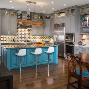 Cette photo montre une cuisine américaine éclectique en L avec un placard avec porte à panneau encastré, des portes de placard turquoises, une crédence multicolore, un électroménager en acier inoxydable, un sol en bois brun, un îlot central, un sol marron et un plan de travail gris.