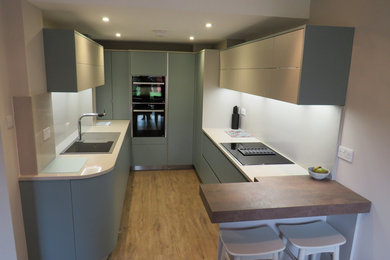 Small contemporary u-shaped enclosed kitchen in Essex with a built-in sink, flat-panel cabinets, green cabinets, quartz worktops, beige splashback, black appliances, light hardwood flooring, no island, brown floors and beige worktops.