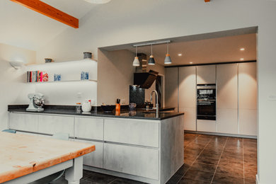 Photo of a large modern u-shaped kitchen/diner in Surrey with a single-bowl sink, flat-panel cabinets, grey cabinets, quartz worktops, black appliances and black worktops.