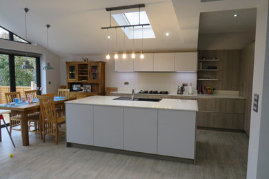 Exempel på ett stort modernt vit vitt kök med öppen planlösning, med en enkel diskho, släta luckor, skåp i ljust trä, bänkskiva i kvartsit, vitt stänkskydd, stänkskydd i sten, svarta vitvaror, ljust trägolv, en köksö och beiget golv