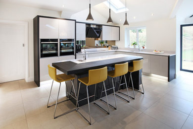 Design ideas for a contemporary kitchen in Manchester with a submerged sink, flat-panel cabinets, white cabinets, glass sheet splashback, black appliances and an island.