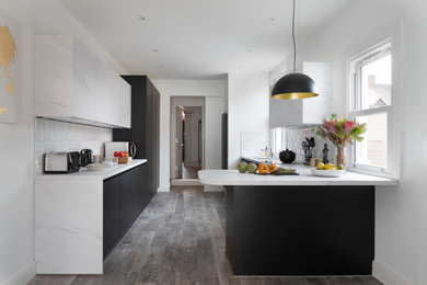 Inspiration for a medium sized contemporary u-shaped kitchen/diner in Oxfordshire with a single-bowl sink, flat-panel cabinets, white cabinets, laminate countertops, yellow splashback, ceramic splashback, black appliances, laminate floors, a breakfast bar, grey floors and white worktops.