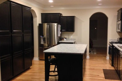Example of a light wood floor kitchen design in Columbus with an island, recessed-panel cabinets, dark wood cabinets, laminate countertops, stainless steel appliances and a drop-in sink