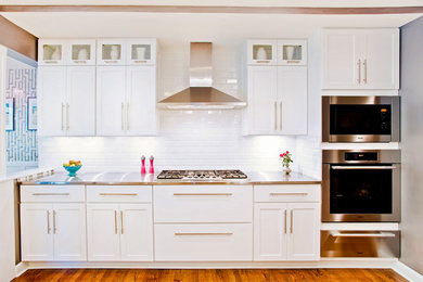 Inspiration for a mid-sized transitional l-shaped medium tone wood floor eat-in kitchen remodel in Chicago with an undermount sink, shaker cabinets, white cabinets, stainless steel countertops, white backsplash, subway tile backsplash, stainless steel appliances and a peninsula