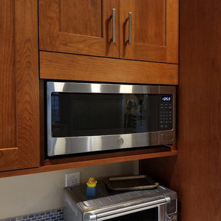Mid-sized transitional l-shaped eat-in kitchen in DC Metro with an integrated sink, recessed-panel cabinets, medium wood cabinets, solid surface benchtops, blue splashback, mosaic tile splashback, stainless steel appliances, medium hardwood floors, a peninsula, brown floor and blue benchtop.