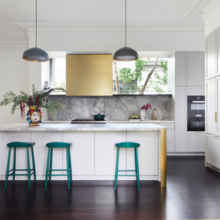 This is an example of a mid-sized transitional open plan kitchen in Melbourne with a double-bowl sink, white cabinets, marble benchtops, multi-coloured splashback, marble splashback, black appliances, dark hardwood floors, with island, brown floor, white benchtop and shaker cabinets.
