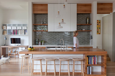 This is an example of a large contemporary galley kitchen in Melbourne with a built-in sink, flat-panel cabinets, medium wood cabinets, wood worktops, grey splashback, stainless steel appliances, light hardwood flooring, an island and metro tiled splashback.