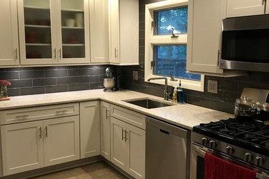 Example of a mid-sized transitional l-shaped gray floor eat-in kitchen design in New York with an undermount sink, shaker cabinets, white cabinets, granite countertops, gray backsplash and stainless steel appliances