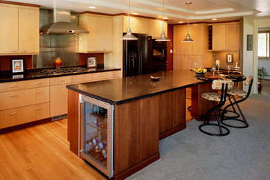 This is an example of a medium sized contemporary l-shaped kitchen/diner in Denver with a submerged sink, flat-panel cabinets, light wood cabinets, granite worktops, green splashback, glass tiled splashback, black appliances, medium hardwood flooring, an island and brown floors.