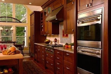 Eat-in kitchen - galley medium tone wood floor eat-in kitchen idea in Atlanta with recessed-panel cabinets, dark wood cabinets, granite countertops, stainless steel appliances and an island