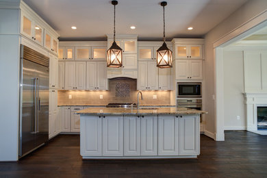 Example of a mid-sized arts and crafts l-shaped dark wood floor and brown floor enclosed kitchen design in DC Metro with an undermount sink, raised-panel cabinets, white cabinets, stainless steel appliances and an island