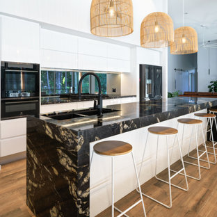 Design ideas for a contemporary galley kitchen in Sunshine Coast with an undermount sink, flat-panel cabinets, white cabinets, window splashback, black appliances, dark hardwood floors, with island, brown floor and black benchtop.