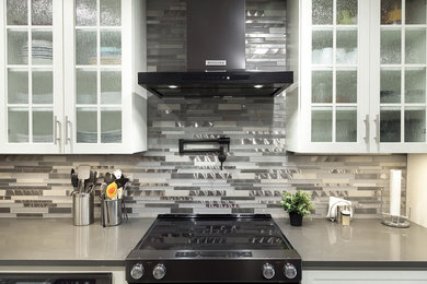 Inredning av ett klassiskt mellanstort grå grått kök, med en undermonterad diskho, skåp i shakerstil, vita skåp, bänkskiva i kvarts, grått stänkskydd, stänkskydd i glaskakel, svarta vitvaror, klinkergolv i porslin, en köksö och grått golv