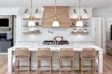Beach style light wood floor and beige floor kitchen photo in Minneapolis with a farmhouse sink, shaker cabinets, white cabinets, marble countertops, white backsplash, subway tile backsplash, stainless steel appliances, an island and white countertops