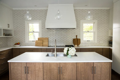 Photo of a large contemporary u-shaped kitchen/diner in Chicago with a submerged sink, flat-panel cabinets, medium wood cabinets, engineered stone countertops, white splashback, metro tiled splashback, stainless steel appliances, medium hardwood flooring, an island and brown floors.
