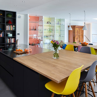 This is an example of a large contemporary single-wall open plan kitchen with flat-panel cabinets, an island, grey floors, black cabinets, stainless steel worktops, yellow splashback, glass sheet splashback, stainless steel appliances and ceramic flooring.
