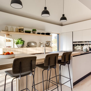 Photo of a medium sized contemporary single-wall kitchen in Gloucestershire with a submerged sink, flat-panel cabinets, white cabinets, black appliances, light hardwood flooring, an island, multicoloured worktops and beige floors.