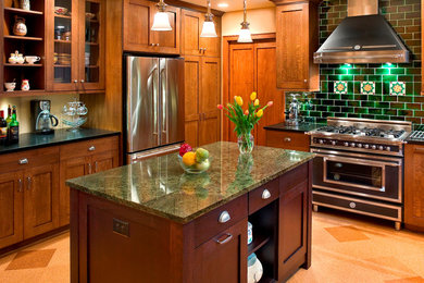 Example of a large arts and crafts u-shaped cork floor enclosed kitchen design in Other with a farmhouse sink, recessed-panel cabinets, medium tone wood cabinets, granite countertops, green backsplash, porcelain backsplash, an island and stainless steel appliances
