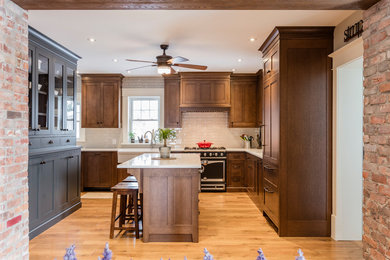 Mid-sized farmhouse l-shaped light wood floor and beige floor eat-in kitchen photo in Toronto with an island, shaker cabinets, dark wood cabinets, a farmhouse sink, marble countertops, white backsplash, subway tile backsplash and black appliances