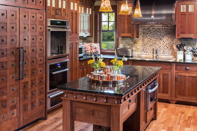 Inspiration for a large timeless u-shaped dark wood floor eat-in kitchen remodel in Milwaukee with a farmhouse sink, recessed-panel cabinets, medium tone wood cabinets, granite countertops, brown backsplash, stone tile backsplash, paneled appliances and two islands