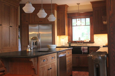 Example of a mid-sized arts and crafts l-shaped medium tone wood floor eat-in kitchen design in Other with a farmhouse sink, shaker cabinets, medium tone wood cabinets, soapstone countertops, white backsplash, subway tile backsplash, stainless steel appliances and an island